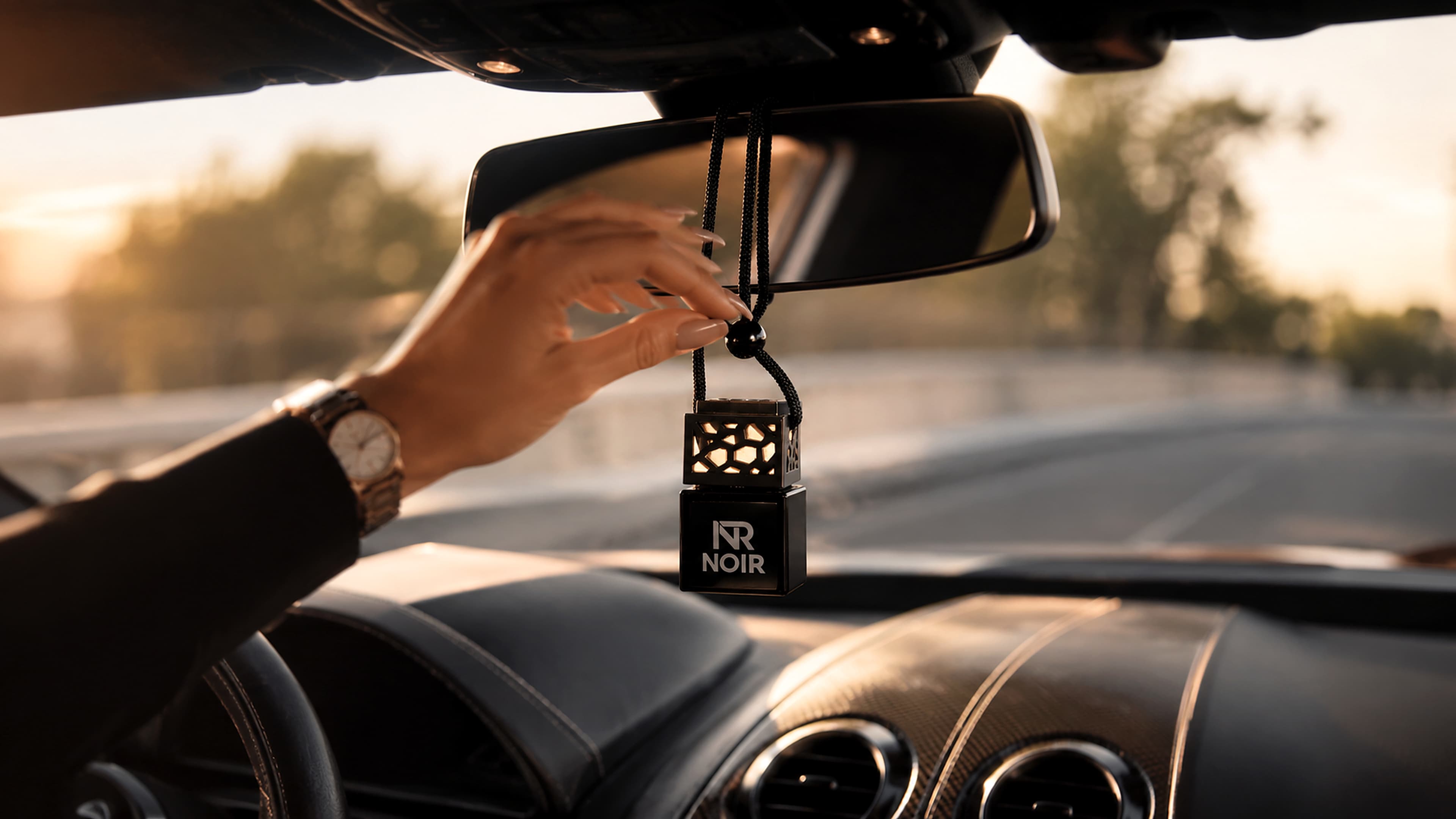 A hand placing the Noir Moris diffuser on a car rearview mirror at golden hour